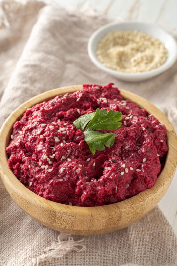 roasted beet hummus in wooden bowl with sesame seeds as garnish