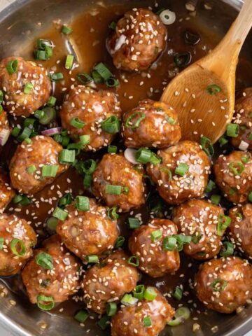 Asian meatballs in a pan of sauce with sesame seeds and green onions