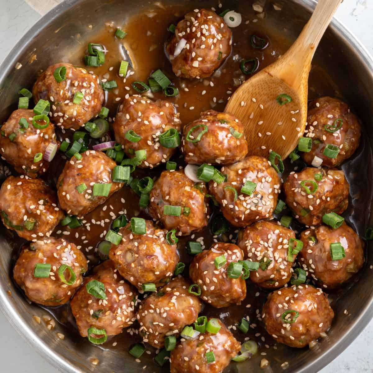 Asian meatballs in a pan of sauce with sesame seeds and green onions